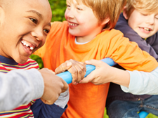 Auf dem Bild sind vier Kinder zu sehen, die auf einem Klettergerüst spielen. Sie lachen. Im Hintergrund ist eine grüne Hecke zu sehen.