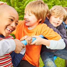 Auf dem Bild sind vier Kinder zu sehen, die auf einem Klettergerüst spielen. Sie lachen. Im Hintergrund ist eine grüne Hecke zu sehen.