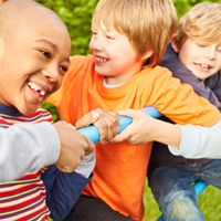 Auf dem Bild sind vier Kinder zu sehen, die auf einem Klettergerüst spielen. Sie lachen. Im Hintergrund ist eine grüne Hecke zu sehen.