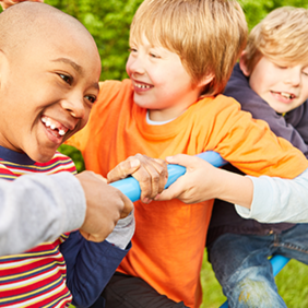 Auf dem Bild sind vier Kinder zu sehen, die auf einem Klettergerüst spielen. Sie lachen. Im Hintergrund ist eine grüne Hecke zu sehen.