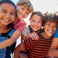 Eine Gruppe von sechs fröhlichen Kindern steht dicht beieinander und lächelt in die Kamera. Sie sind bunt gekleidet. 