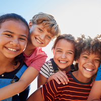 Eine Gruppe von sechs fröhlichen Kindern steht dicht beieinander und lächelt in die Kamera. Sie sind bunt gekleidet. 