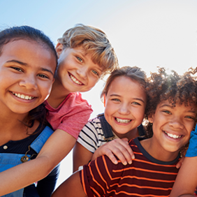 Eine Gruppe von sechs fröhlichen Kindern steht dicht beieinander und lächelt in die Kamera. Sie sind bunt gekleidet. 