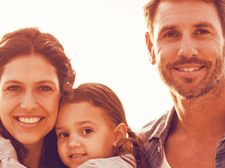 Auf dem Bild ist eine Familie. Links steht die Frau, hat das Mädchen auf dem Arm. Rechts steht ein Mann, der Frau mit Kind zugewandt.