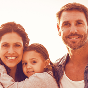 Auf dem Bild ist eine Familie. Links steht die Frau, hat das Mädchen auf dem Arm. Rechts steht ein Mann, der Frau mit Kind zugewandt.