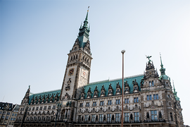 Das Bild zeigt das Hamburger Rathaus. Der Himmel im Hintergrund ist klar und blau, was das Gebäude eindrucksvoll erscheinen lässt. Das Bild ist aus der Froschperspektive gemacht.