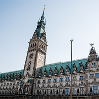 Das Bild zeigt das Hamburger Rathaus. Der Himmel im Hintergrund ist klar und blau, was das Gebäude eindrucksvoll erscheinen lässt. Das Bild ist aus der Froschperspektive gemacht.