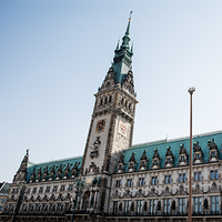 Das Bild zeigt das Hamburger Rathaus. Der Himmel im Hintergrund ist klar und blau, was das Gebäude eindrucksvoll erscheinen lässt. Das Bild ist aus der Froschperspektive gemacht.