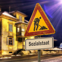 Das Bild zeigt ein altes, beleuchtetes Gebäude bei Nacht. Im Vordergrund steht ein Verkehrsschild mit einem Baustellensymbol, das einen Arbeiter zeigt, der mit einer Schaufel arbeitet. Unter dem Baustellensymbol befindet sich ein weiteres Schild mit der Aufschrift "Sozialstaat". 