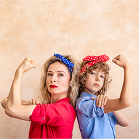 Zwei Frauen, die Rücken an Rücken stehen und ihre Arme in einer starken Pose beugen. Beide tragen bunte Haarbänder – eine Person trägt ein blaues Kopftuch mit weißen Punkten, die andere ein rotes Kopftuch mit weißen Punkten. Die Person links trägt ein rotes Hemd, während die Person rechts ein blaues Hemd trägt. Der Hintergrund ist neutral beige gehalten. Die beiden Personen schauen entschlossen in die Kamera.