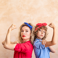 Zwei Frauen, die Rücken an Rücken stehen und ihre Arme in einer starken Pose beugen. Beide tragen bunte Haarbänder – eine Person trägt ein blaues Kopftuch mit weißen Punkten, die andere ein rotes Kopftuch mit weißen Punkten. Die Person links trägt ein rotes Hemd, während die Person rechts ein blaues Hemd trägt. Der Hintergrund ist neutral beige gehalten. Die beiden Personen schauen entschlossen in die Kamera.