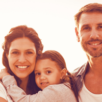 Auf dem Bild ist eine Familie. Links steht die Frau, hat das Mädchen auf dem Arm. Rechts steht ein Mann, der Frau mit Kind zugewandt.