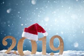 Das Bild zeigt die goldenen Zahlen "2019" auf einer schneebedeckten Fläche. Auf der Zahl "0" sitzt eine rote Weihnachtsmütze mit weißem Rand und Bommel. Im Hintergrund ist ein blauer Himmel zu sehen, durch den Schneeflocken fallen. 