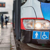 Auf dem Bild hält grade ein Bus des ÖPNV an einer Bushaltestellt. Abgebildert sich die Symbole für Senioren und Rollstuhlfahrer.