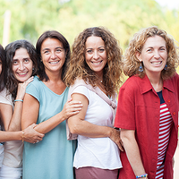 Auf dem Bild stehen sieben Frauen nebeneinander. Alle haben unterschiedlichen Frisuren und unterschiedliche Kleidnug an. Alle lachen und sind fröhlich und gucken nach vorne.