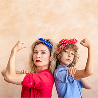 Zwei Frauen, die Rücken an Rücken stehen und ihre Arme in einer starken Pose beugen. Beide tragen bunte Haarbänder – eine Person trägt ein blaues Kopftuch mit weißen Punkten, die andere ein rotes Kopftuch mit weißen Punkten. Die Person links trägt ein rotes Hemd, während die Person rechts ein blaues Hemd trägt. Der Hintergrund ist neutral beige gehalten. Die beiden Personen schauen entschlossen in die Kamera.