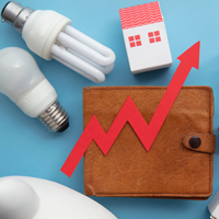 Das Bild zeigt eine braune Geldbörse, auf der ein roter Pfeil in Form eines steigenden Diagramms platziert ist. Um die Geldbörse herum sind verschiedene Gegenstände angeordnet: zwei Glühbirnen, ein Miniatur-Einkaufswagen und zwei kleine Häuser. Der Hintergrund ist hellblau. Das Bild symbolisiert steigende Kosten oder Preise in verschiedenen Lebensbereichen wie Energie, Wohnen und Konsumgüter.
