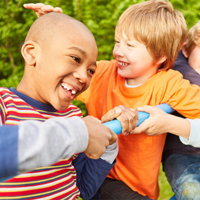 Auf dem Bild sind vier Kinder zu sehen, die auf einem Klettergerüst spielen. Sie lachen. Im Hintergrund ist eine grüne Hecke zu sehen.