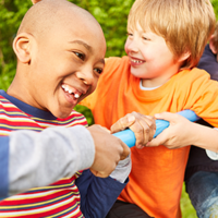 Auf dem Bild sind vier Kinder zu sehen, die auf einem Klettergerüst spielen. Sie lachen. Im Hintergrund ist eine grüne Hecke zu sehen.