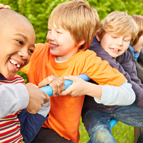 Auf dem Bild sind vier Kinder zu sehen, die auf einem Klettergerüst spielen. Sie lachen. Im Hintergrund ist eine grüne Hecke zu sehen.