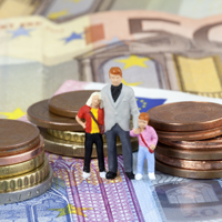 Das Bild zeigt drei Miniaturfiguren, die eine Familie darstellen, bestehend aus einem Erwachsenen und zwei Kindern. Sie stehen auf einem Haufen von Euro-Münzen und -Scheinen. Die Münzen sind in verschiedenen Größen gestapelt, und die Scheine sind im Hintergrund sichtbar. 
