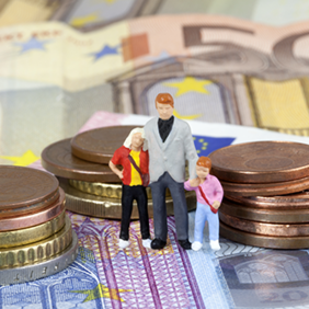 Das Bild zeigt drei Miniaturfiguren, die eine Familie darstellen, bestehend aus einem Erwachsenen und zwei Kindern. Sie stehen auf einem Haufen von Euro-Münzen und -Scheinen. Die Münzen sind in verschiedenen Größen gestapelt, und die Scheine sind im Hintergrund sichtbar.