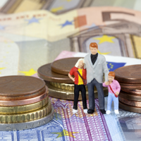 Das Bild zeigt drei Miniaturfiguren, die eine Familie darstellen, bestehend aus einem Erwachsenen und zwei Kindern. Sie stehen auf einem Haufen von Euro-Münzen und -Scheinen. Die Münzen sind in verschiedenen Größen gestapelt, und die Scheine sind im Hintergrund sichtbar. 