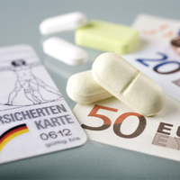 Auf dem Bild sind eine Krankenversicherungskarte, mehrere Euro-Banknoten und -Münzen sowie einige Tabletten zu sehen. Die Krankenversicherungskarte liegt links im Vordergrund, während die Banknoten und Münzen rechts daneben platziert sind. Die Tabletten befinden sich in der Mitte des Bildes.
