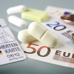 Auf dem Bild sind eine Krankenversicherungskarte, mehrere Euro-Banknoten und -Münzen sowie einige Tabletten zu sehen. Die Krankenversicherungskarte liegt links im Vordergrund, während die Banknoten und Münzen rechts daneben platziert sind. Die Tabletten befinden sich in der Mitte des Bildes.