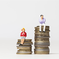 Das Bild zeigt zwei Miniaturfiguren, die auf gestapelten Münzen sitzen. Die linke Figur trägt eine rote Jacke und einen gelben Hut und sitzt auf einem kleineren Stapel Münzen. Die rechte Figur trägt ein lila Oberteil und weiße Hosen und sitzt auf einem höheren Stapel Münzen. Der Hintergrund ist schlicht und weiß.