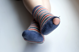 Das Bild zeigt ein Paar Füße, die in gestreiften Socken stecken. Die Socken haben blaue, rote und weiße Streifen. An einem der Socken ist ein Loch, durch das ein Zeh hervorschaut. 